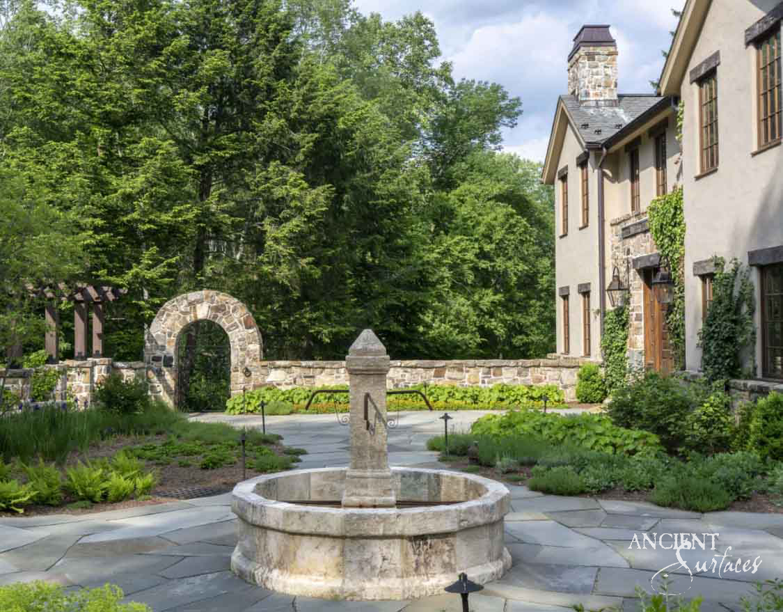 Round cream limestone pool fountain with a square pillar spout in a walled garden